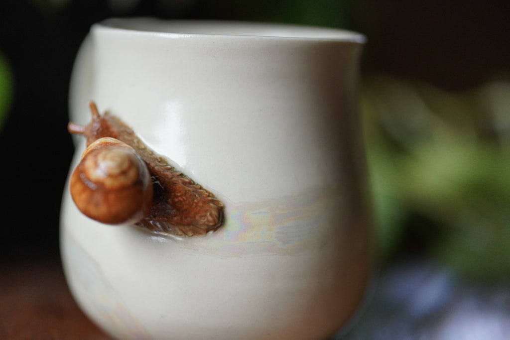 Snail on a white ceramic mug with a blurred green background