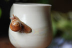 Snail on a white ceramic mug with a blurred green background