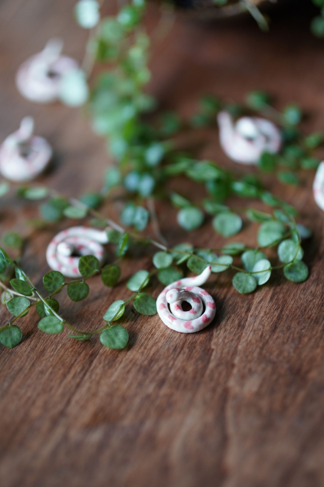Small ceramic snakes on a wooden surface with green leaves.