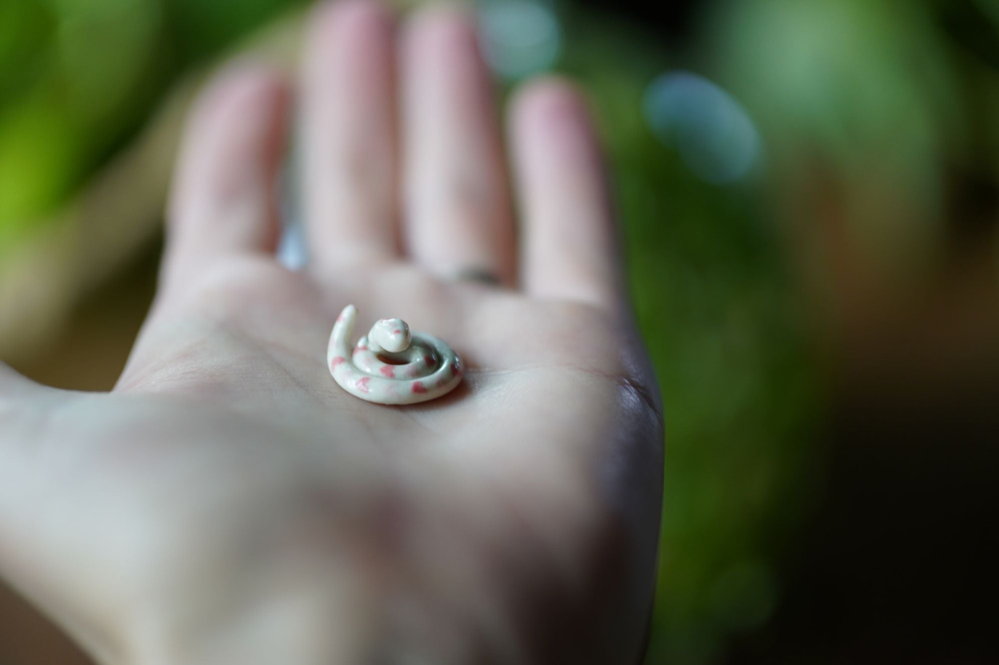 Small snake figurine on a person's palm with a blurred natural background